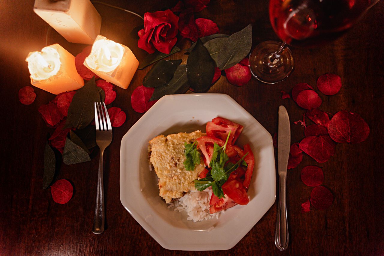 services-01 Romantic table setting with food, candles, and red petals for a cozy dinner.