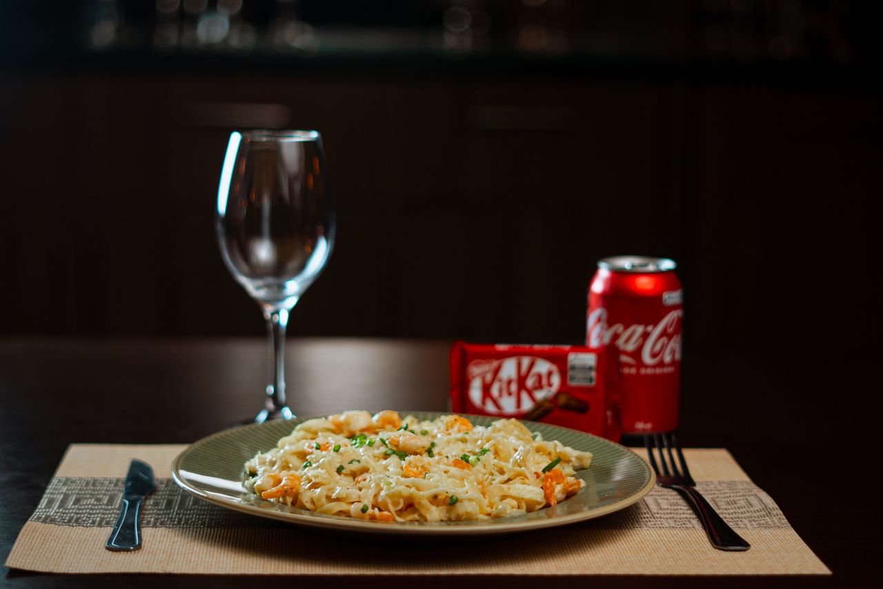 services-img Plate of creamy pasta with Coca-Cola and KitKat, perfect dining setup.