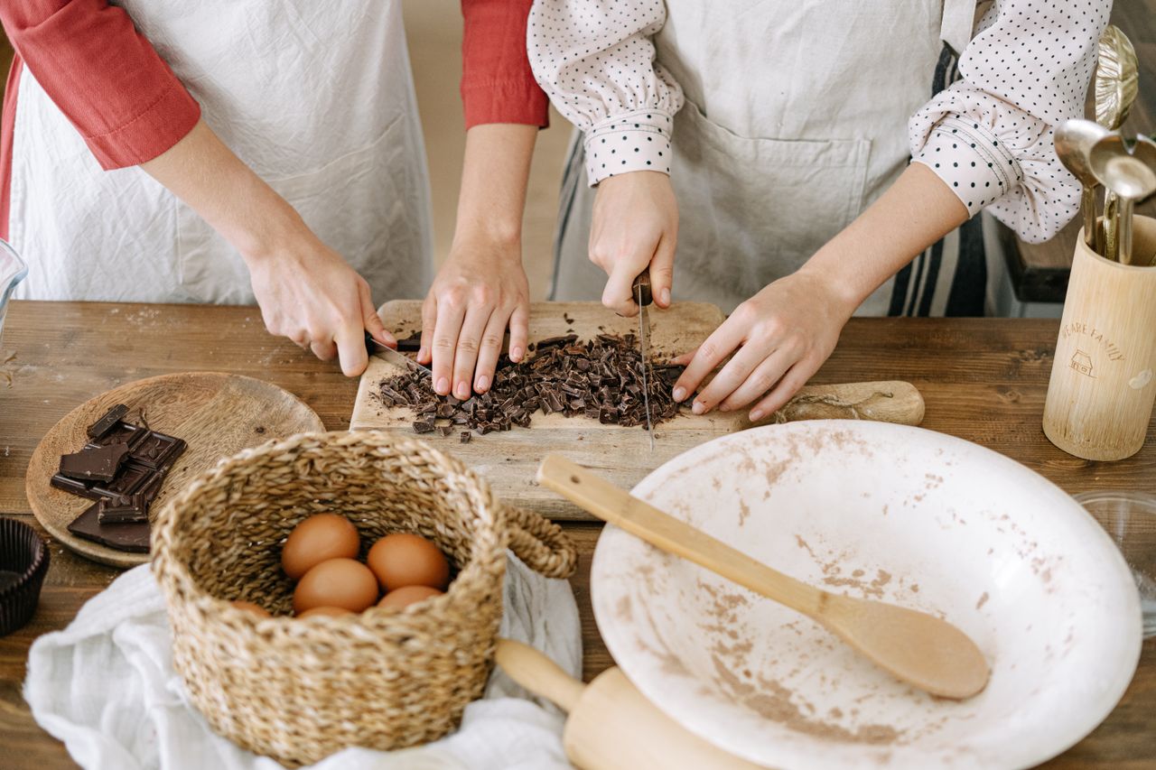 Close-up of hands chopping chocolate with eggs and baking ingredients on a wooden table.