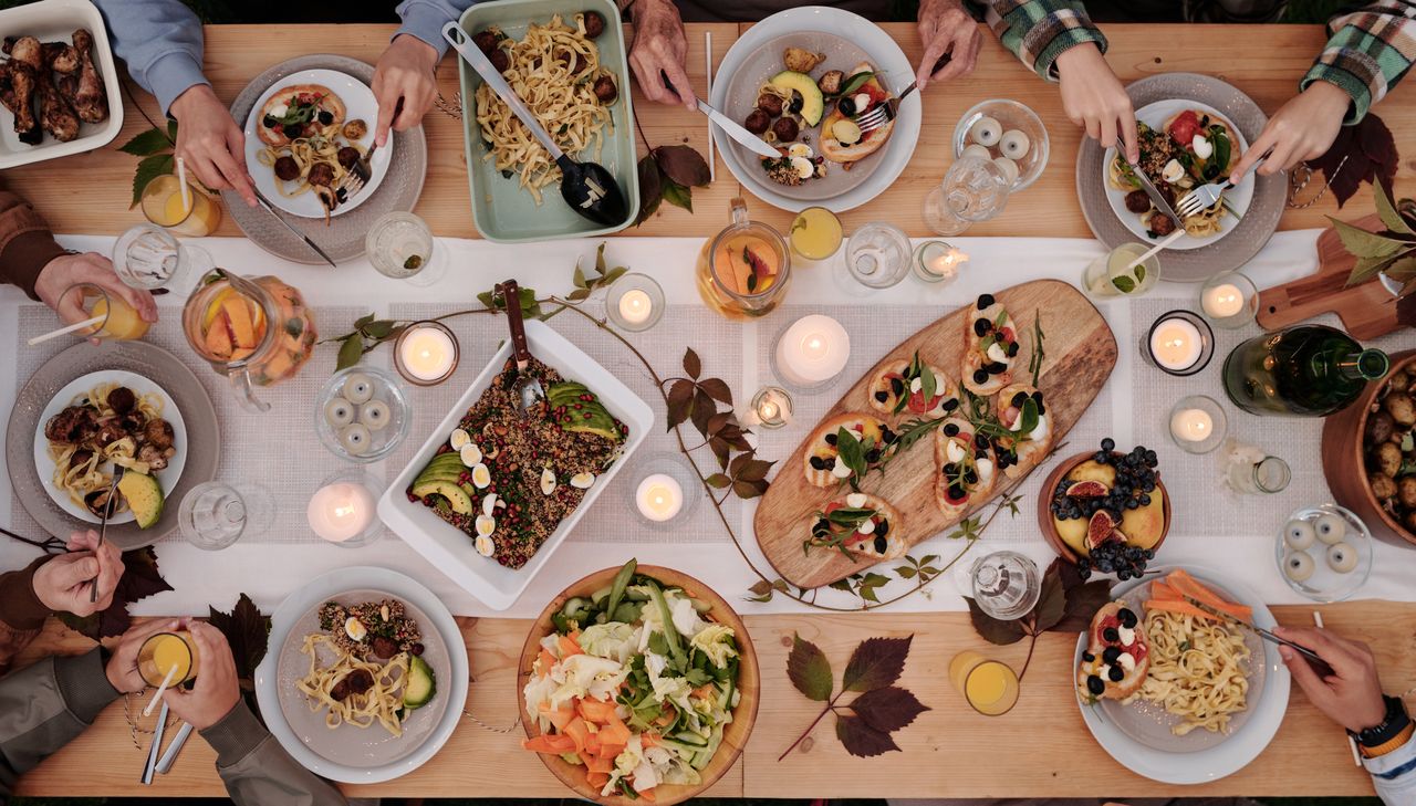 services-01 Overhead shot of a vibrant dining table setup with pasta, salads, and decorative candles, capturing a festive gathering.